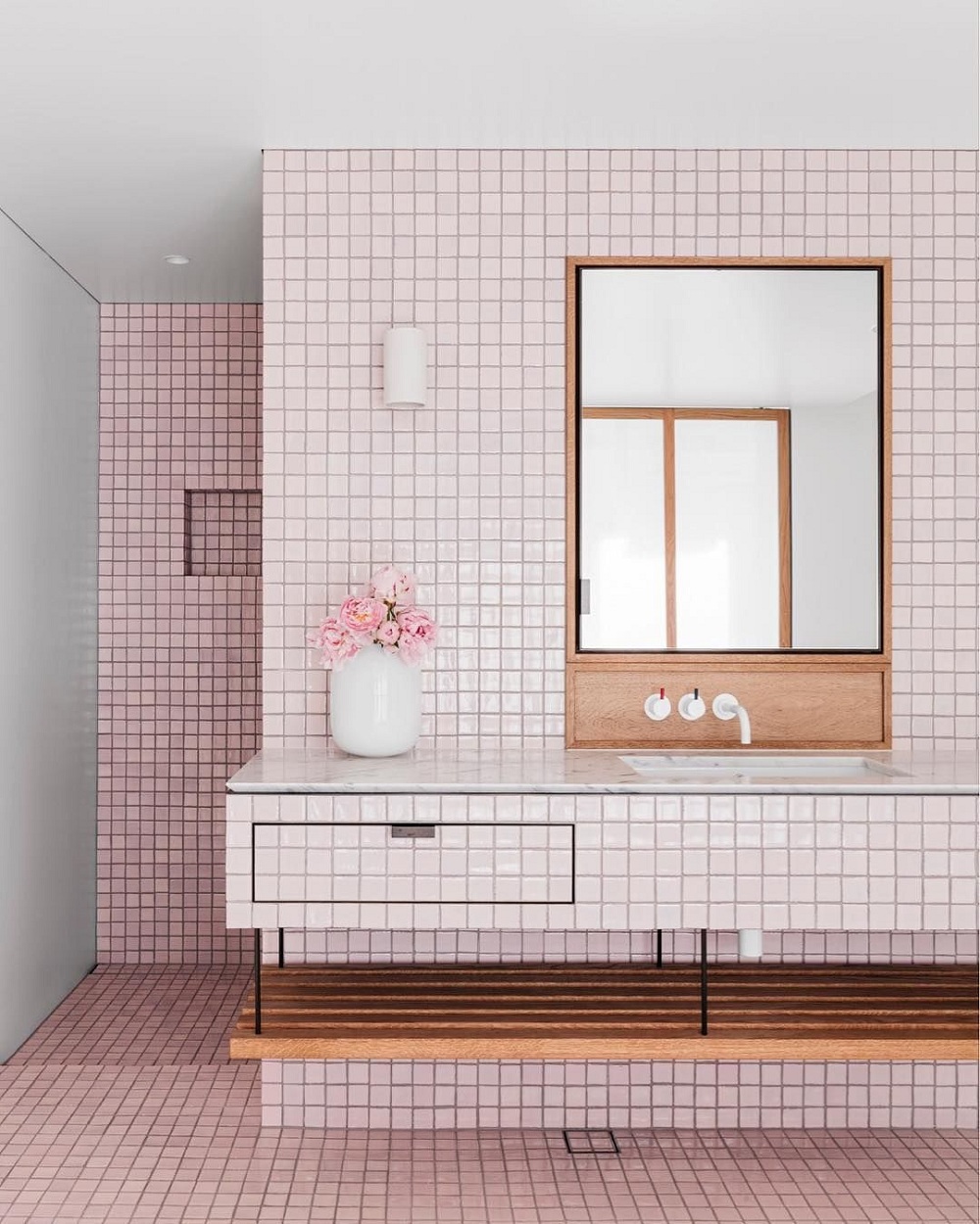 Sắc hồng pastel tạo cảm giác ấm cúng và gần gũi cho phòng tắm khi kết hợp với kệ bằng gỗ và gương thủy tinh.