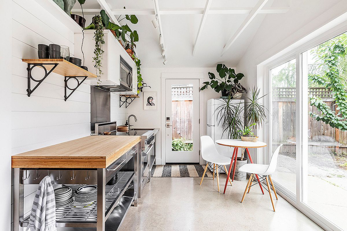 Hình ảnh phòng bếp nhỏ màu trắng, bàn ghế ăn nhỏ xinh, kệ gắn tường và cây xanh trang trí