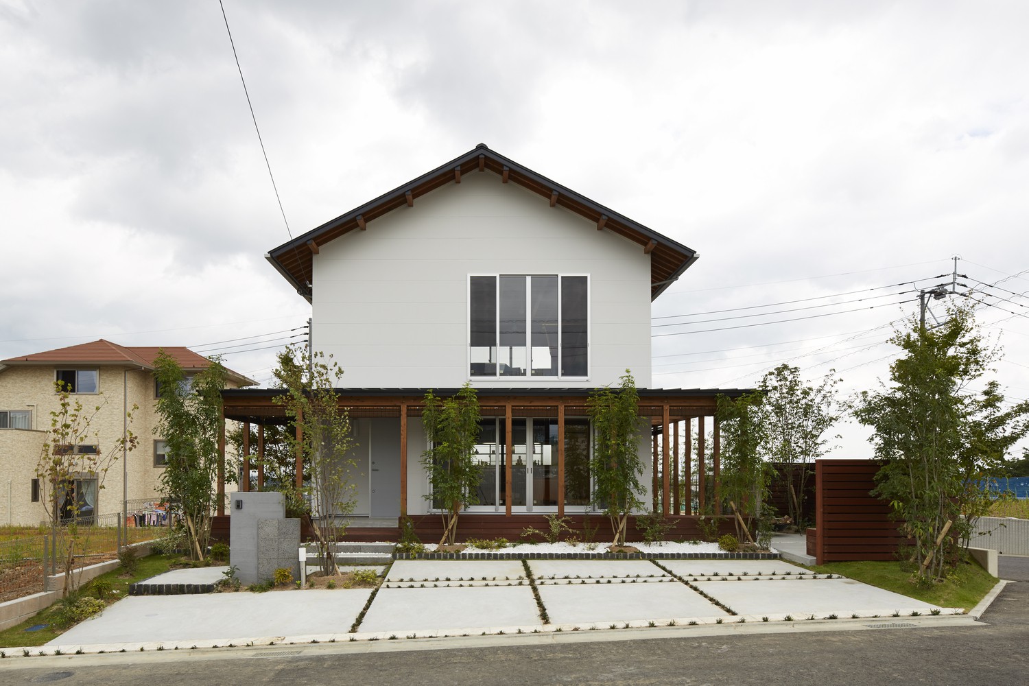 Hình ảnh toàn cảnh ngôi nhà 2 tầng có cấu trúc dạng khung đơn giản, phía trước trồng cây xanh
