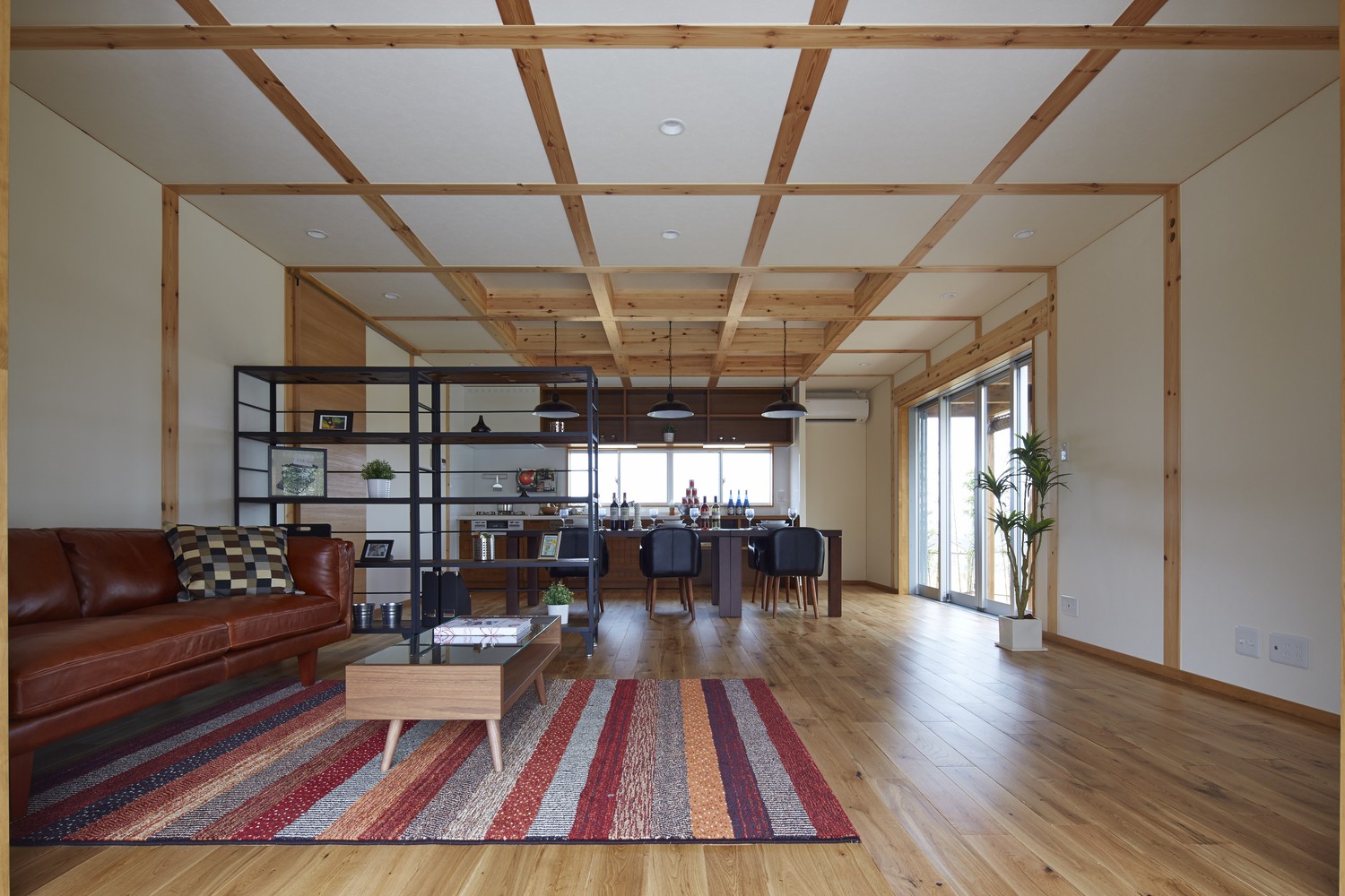 Hình ảnh bên trong nhà 2 tầng với kèo gỗ dạng lưới chịu lực, phòng khách và khu bếp ăn sử dụng nội thất đơn giản