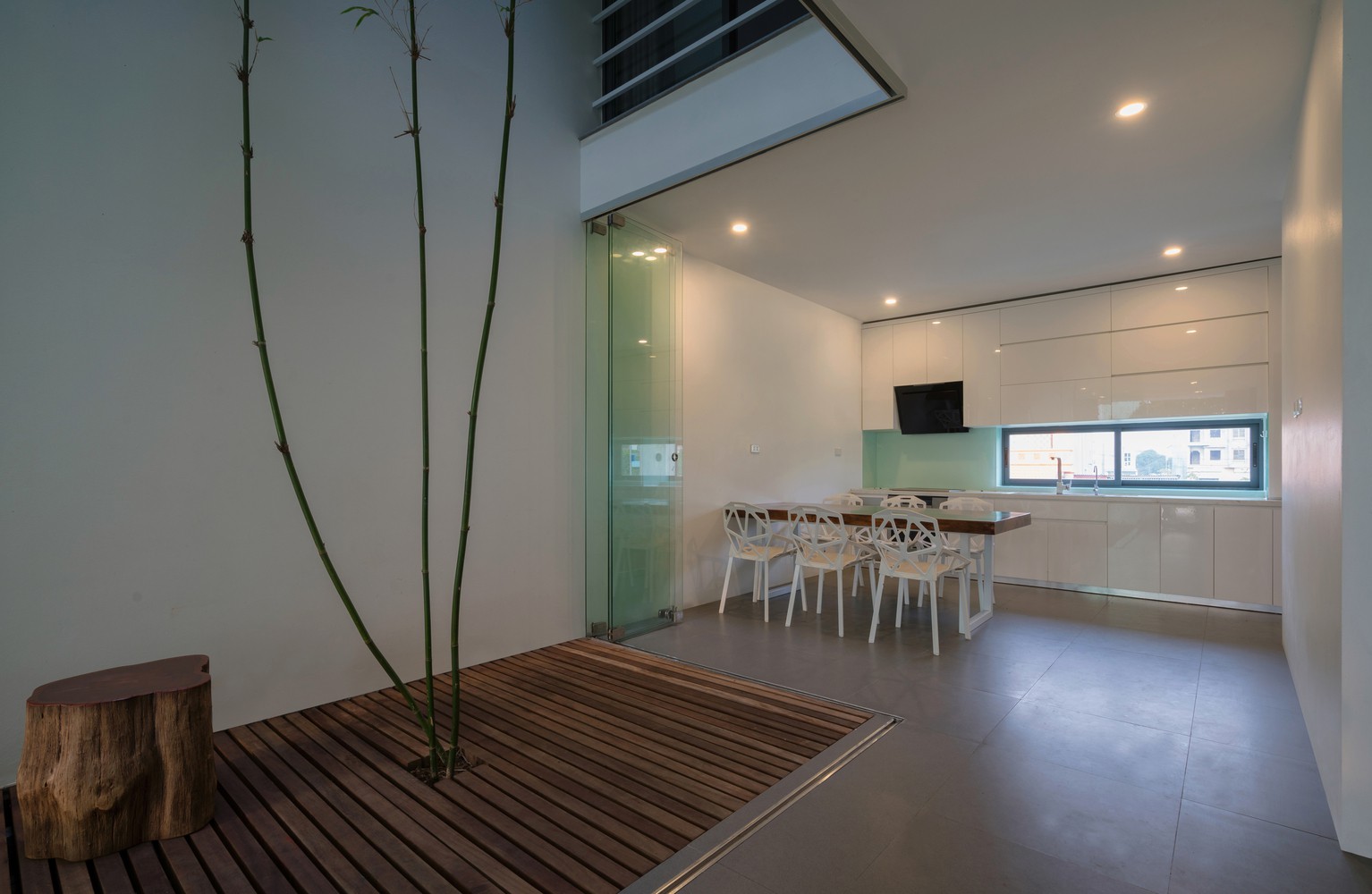 Cạnh khoảng thông tầng nhà phố là không gian ăn uống đơn giản với bàn chữ nhật gắn tường, ghế ngồi màu trắng kiểu dáng hiện đại.