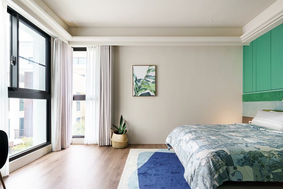 Hình ảnh phòng ngủ thoáng sáng với tường đầu giường sơn xanh lá, chăn nệm họa tiết hoa lá cùng tông với tranh treo tường, rèm cửa màu trắng