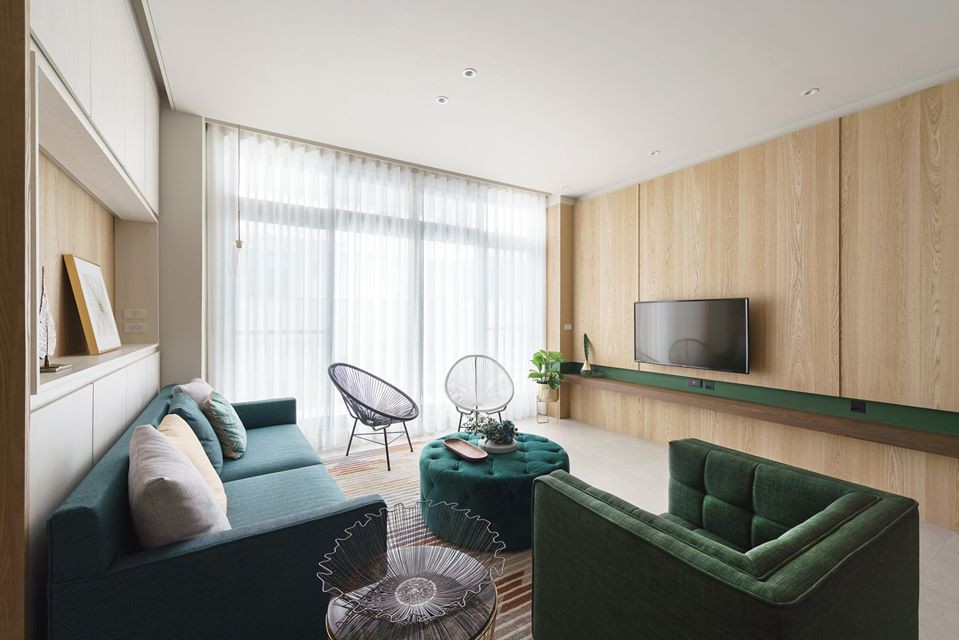 Hình ảnh phòng khách với ghế sofa màu xanh lá, bàn trà đệm, bức tường sau tivi ốp gỗ