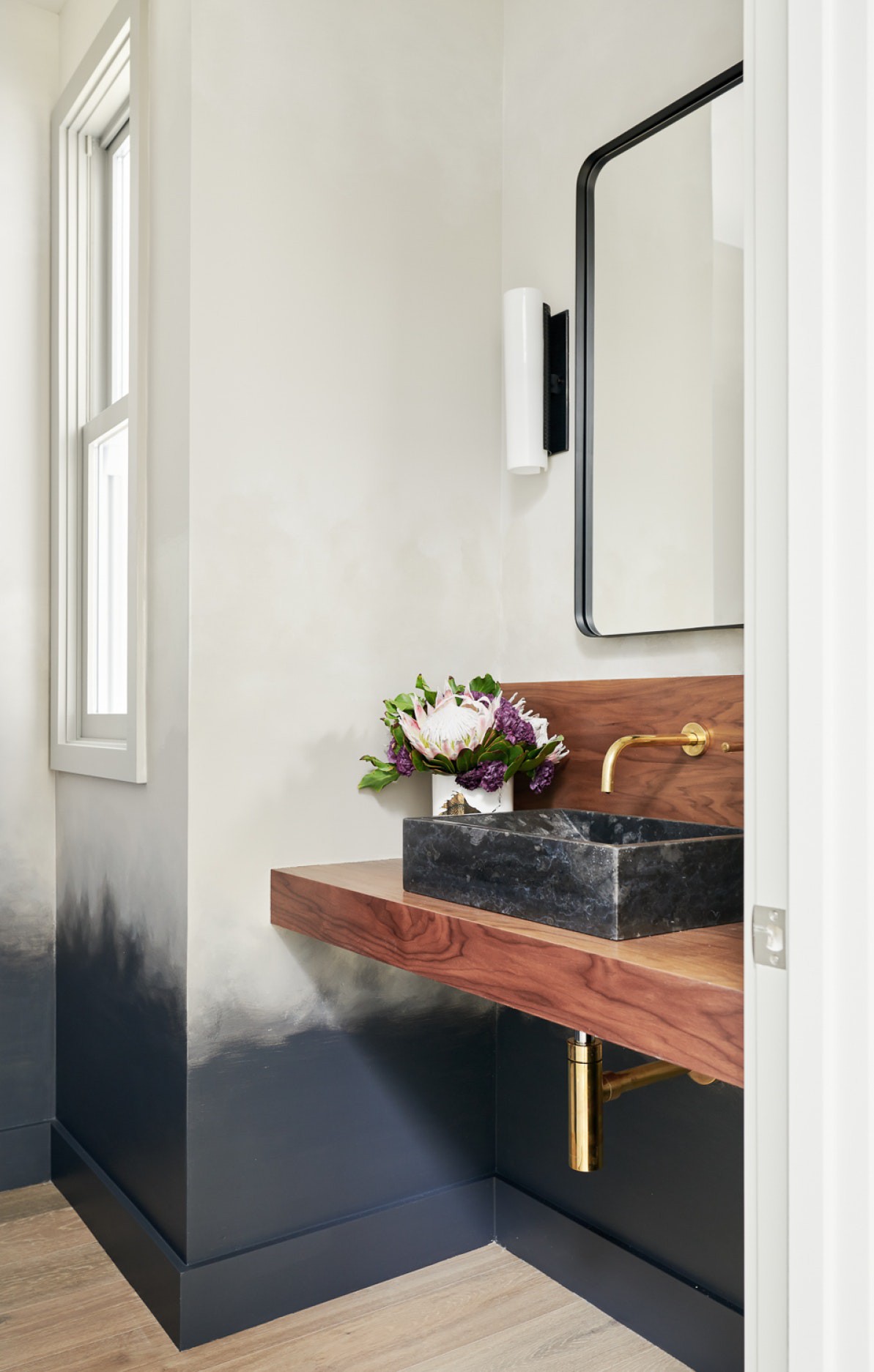 Hình ảnh một góc phòng tắm với bồn rửa làm bằng đá cẩm thạch đen, hài hòa với phân chân tường sơn đen