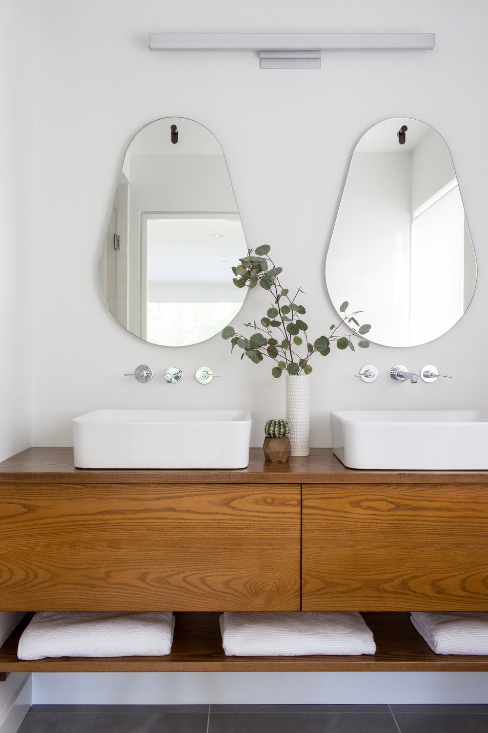 Hình ảnh phòng tắm thanh lịch với bộ đôi bồn rửa bằng sứ màu trắng, hai gương treo phía trên, tủ đựng bằng gỗ