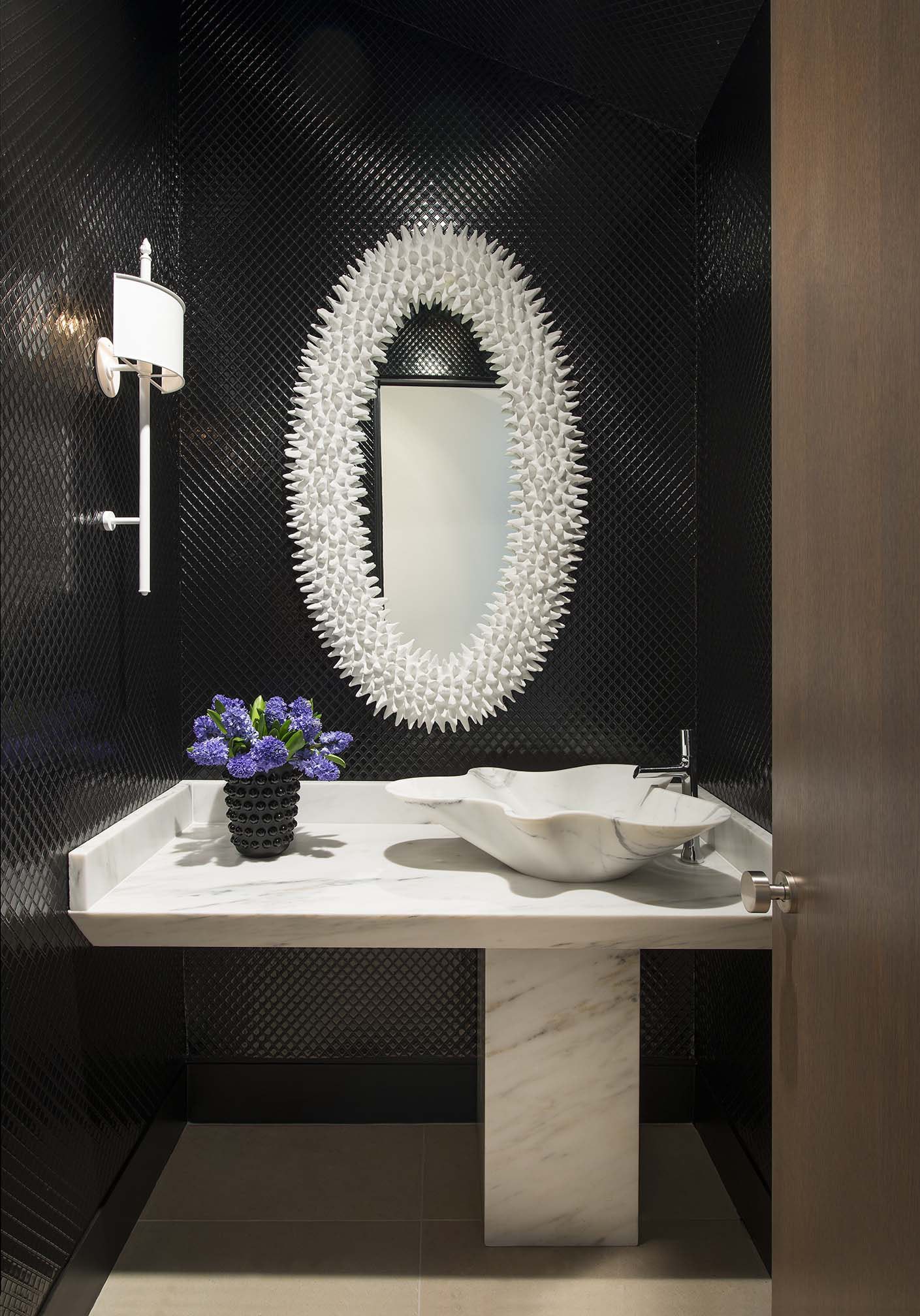 Hình ảnh một góc phòng tắm với bồn rửa bằng đá cẩm thạch trắng, tương phản tường ốp gạch đen, khung gương độc đáo