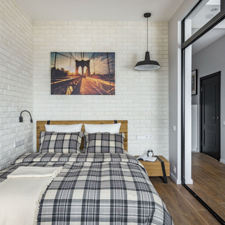 Hình ảnh phòng ngủ với tường gạch sơn trắng, tranh đầu giường, ga gối kẻ sọc, bàn gỗ