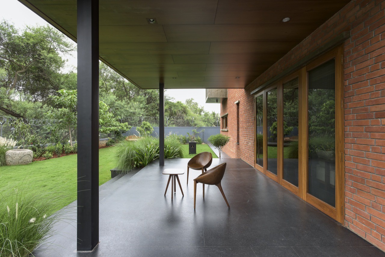 Hình ảnh góc thư giãn nơi hiên nhà với bàn ghế gỗ nhỏ xinh, cạnh đó là sân vườn trồng cây, thảm cỏ