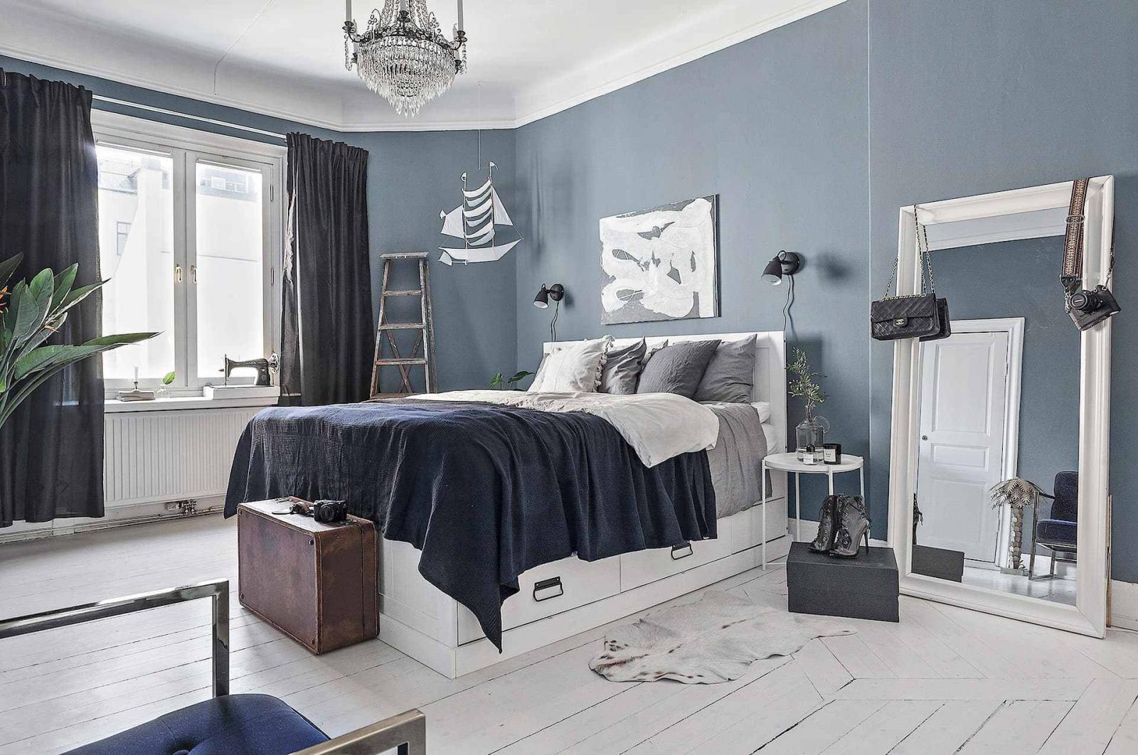 Hình ảnh phòng ngủ rộng rãi với giường nệm êm ái, gương lớn, cửa sổ kính, máy khâu, rèm màu xanh than, tường sơn xanh