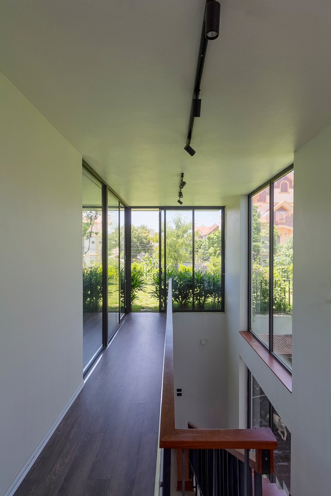 Hình ảnh hành lang nhà 3 tầng được lát gỗ sẫm màu, kết nối với cửa kính hướng nhìn ra  sân vườn xanh mát bên ngoài.
