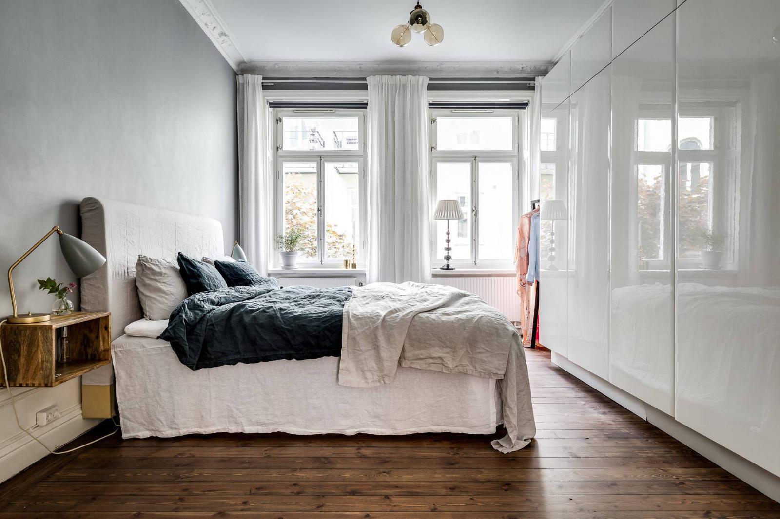 Hình ảnh toàn cảnh phòng ngủ với tủ quần áo âm tường màu trắng, kệ gỗ đầu giường, cửa sổ kính