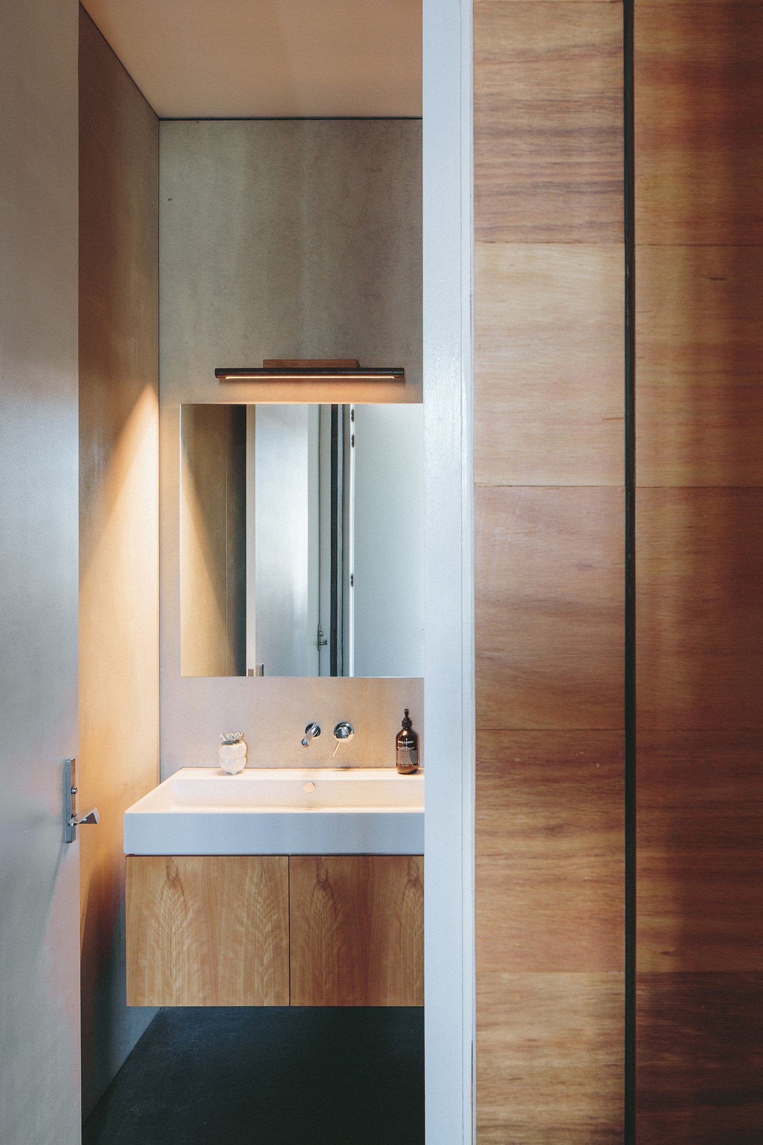 Hình ảnh một góc phòng tắm với bồn rửa sứ trắng, bệ ốp gỗ tự nhiên màu sáng