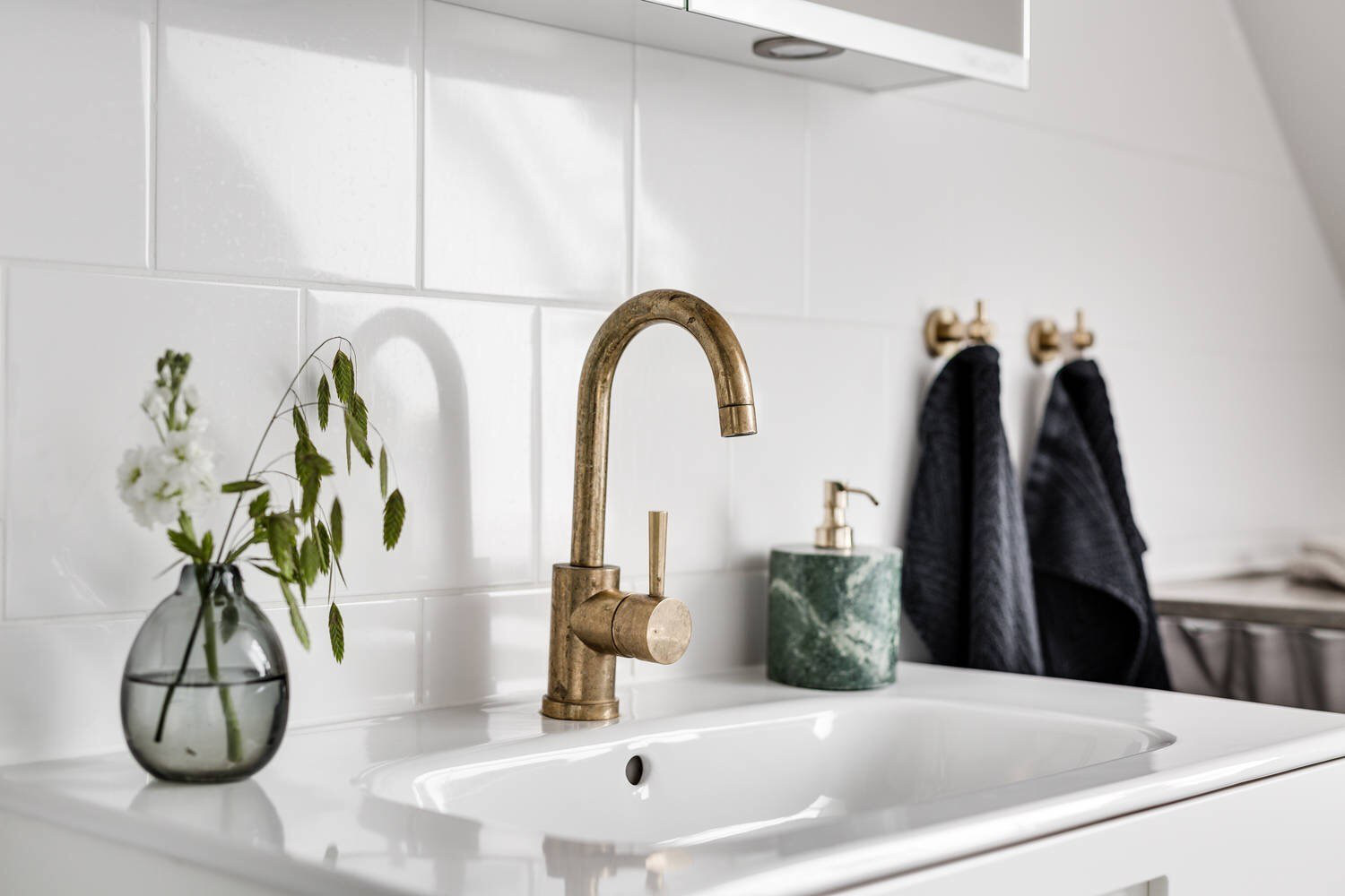 Hình ảnh cận cảnh bình cây thủy tinh trong suốt đặt trên bệ bồn rửa xua tan vẻ đơn điệu của phòng tắm  ​tông màu trắng xám chủ đạo.