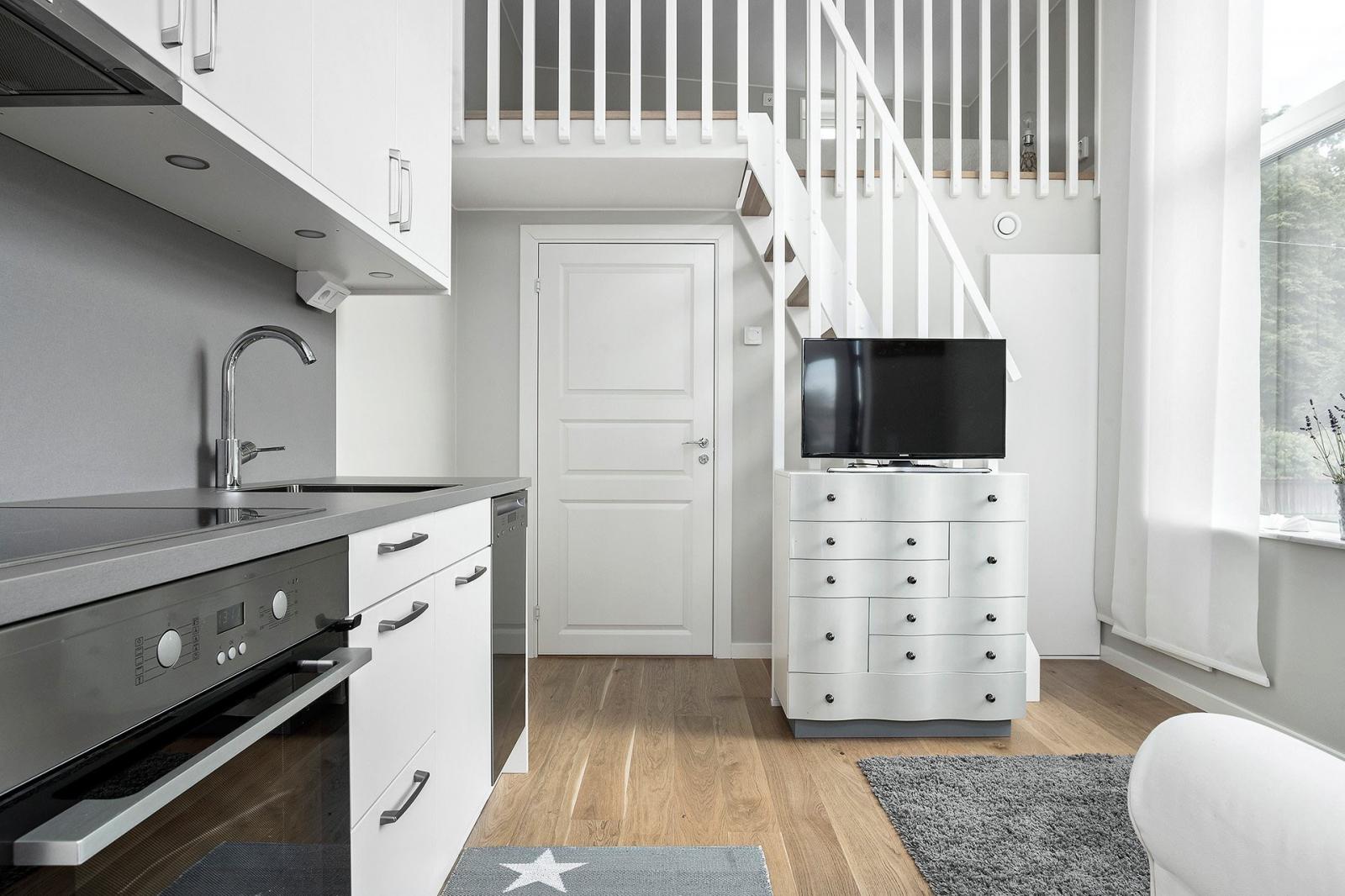 Hình ảnh không gian bên trong nhà nhỏ 19m2 với tủ kệ tivi, sofa màu trắng, bếp nấu, cầu thang lên gác xép