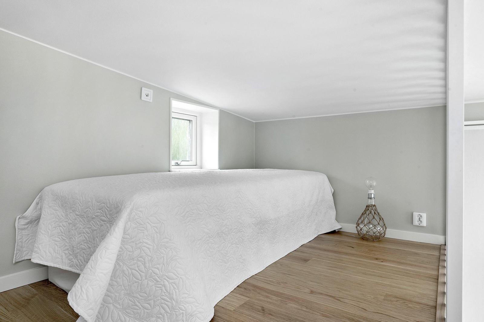 Hình ảnh toàn cảnh phòng ngủ trên gác lửng với sàn lát gỗ, cửa sổ kính, trang trí tối giản