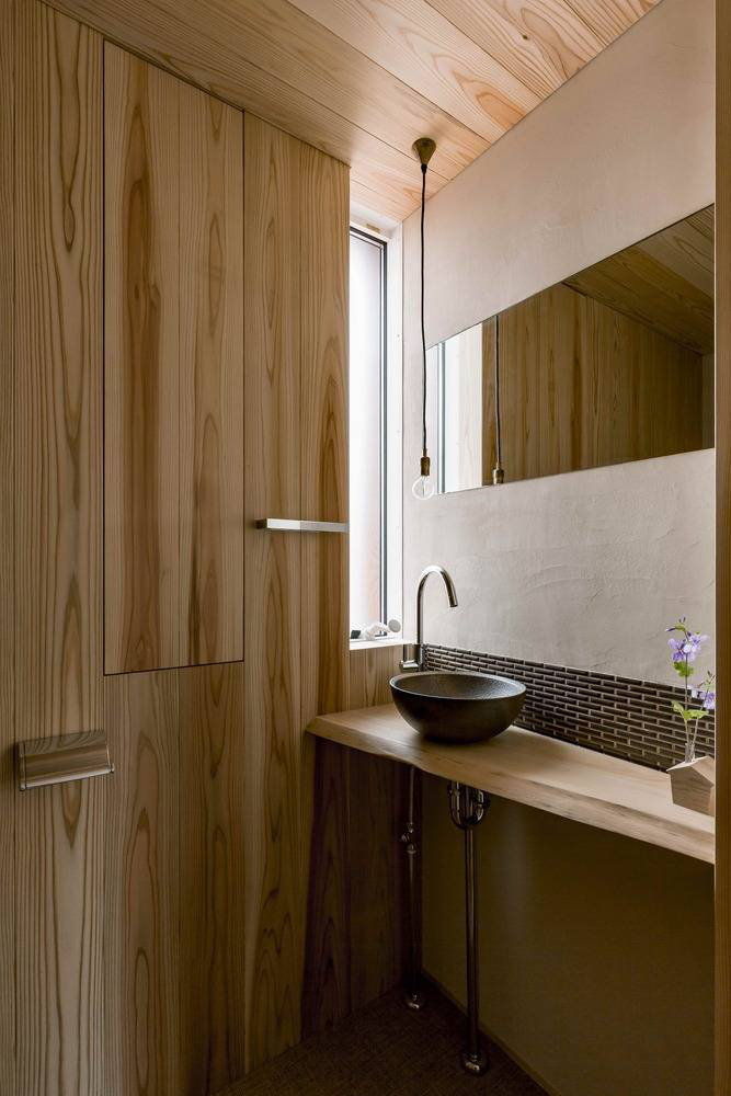 Hình ảnh một góc phòng tắm với tường ốp gỗ còn nguyên đường vân tự nhiên, bồn rửa đá...