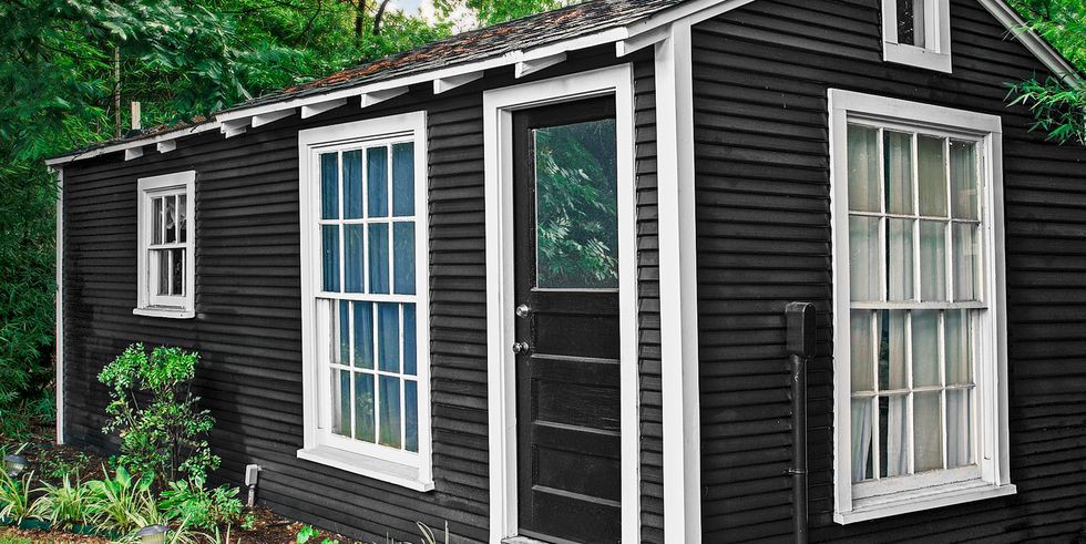 Hình ảnh cận cảnh một ngôi nhà màu đen chủ đạo, cửa sổ trắng, mái ngói, tọa lạc bên cạnh bìa rừng