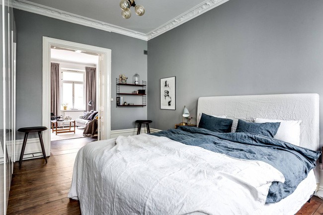 Hình ảnh toàn cảnh phòng ngủ đơn giản với tường, trần màu xám, giường nệm màu trắng, khung tranh trang trí, giá kệ treo tường, đèn chùm sang trọng