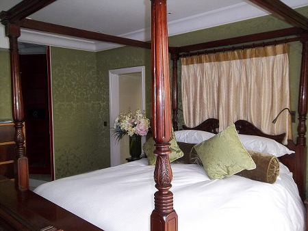Chiếc giường có 4 cột trụ, bằng gỗ sậm màu.