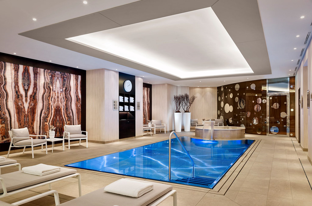 Hình ảnh bể bơi nhỏ trong xanh bên trong khách sạn 5 sao Ritz-Carlton, xung quanh là những chiếc ghế thư giãn êm ái
