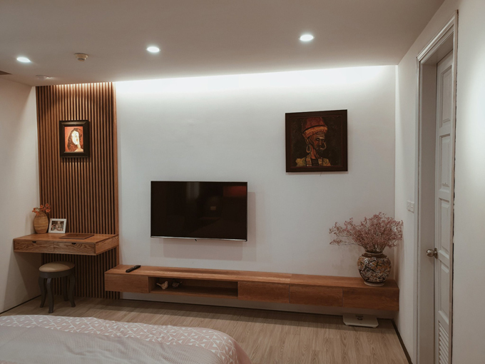 Hình ảnh không gian phòng ngủ chính được bài trí đơn giản với những món nội thất thiết yếu như giường, bàn trang điểm, kệ tivi, trang trí bằng tranh vẽ của chủ nhân.