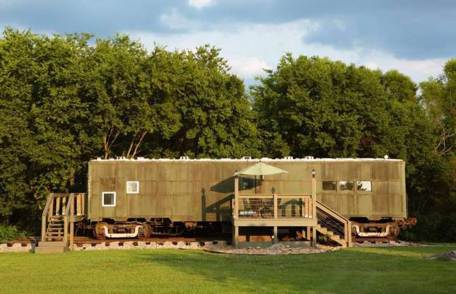 Hình ảnh toàn cảnh một ngôi nhà nghỉ dưỡng được cải tạo từ toa tàu hỏa, đặt trên thảm cỏ xanh mát, phía sau là hàng cây xanh tốt