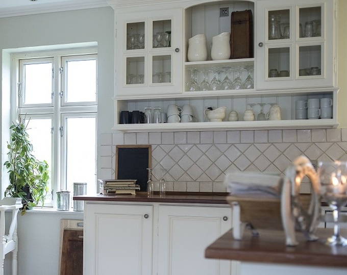 Hình ảnh phòng bếp hiện đại với tủ bếp màu trắng có cửa đóng, cửa sổ kính trong suốt, cây xanh trang trí