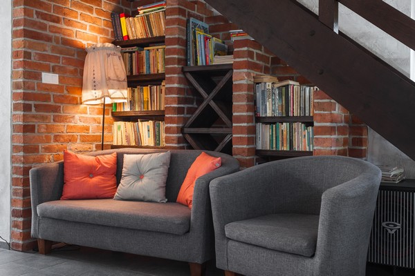 Hình ảnh góc đọc sách ấn tượng với tường gạch nung ấm áp, giá sách sát trần, ghế sofa văng bọc nỉ