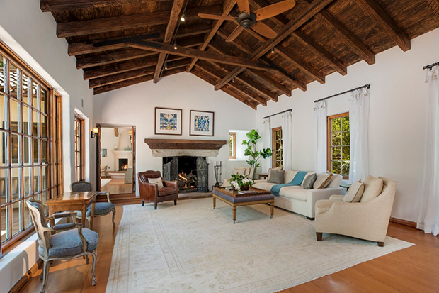 Hình ảnh phòng khách rộng rãi với trần gỗ cao thoáng, cửa sổ kính lớn, lò sưởi và bàn ghế đơn giản