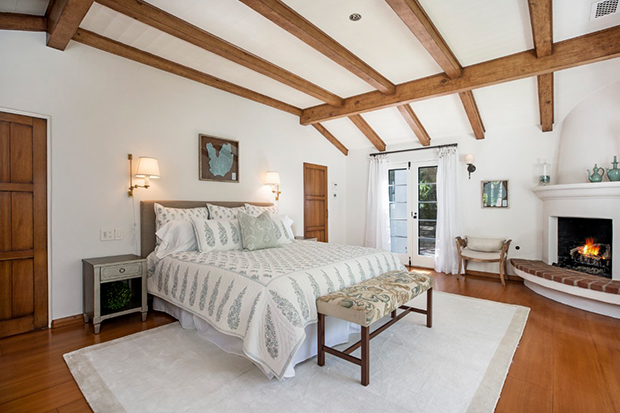 Hình ảnh phòng ngủ chính rộng rãi, tường sơn trắng, trần ốp dầm gỗ, lò sưởi ấm áp