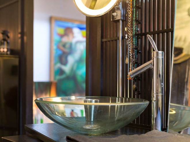 Hình ảnh cận cảnh một góc phòng tắm với bồn rửa mặt bằng kính trong suốt, vòi rửa inox sáng bóng
