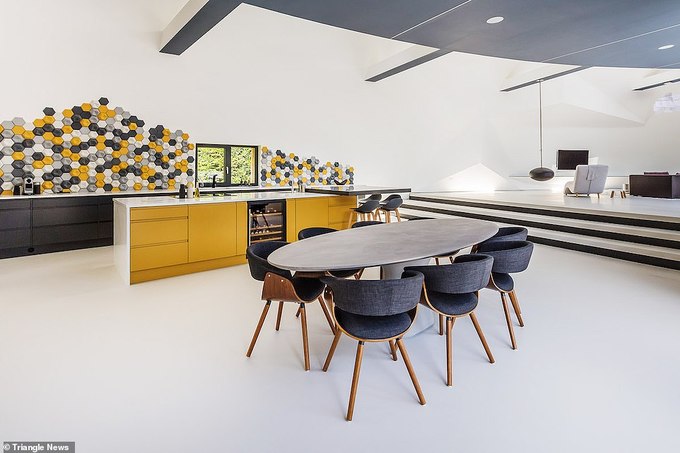Phòng bếp thoáng sáng với bàn ăn hình e líp, đảo bếp màu vàng, quạt trần, tường ốp gạch hình tổ ong