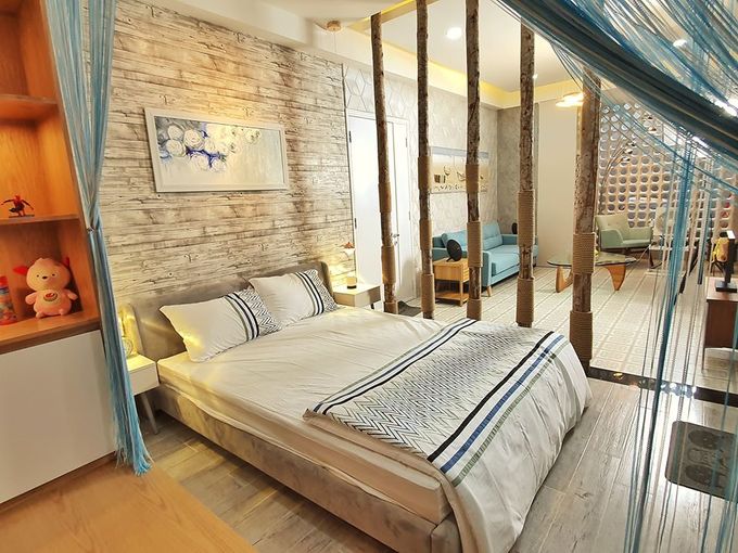 Hình ảnh phòng ngủ với ga gối màu trắng, đầu giường ốp gạch giả gỗ, màn xanh dương, tủ kệ gỗ 