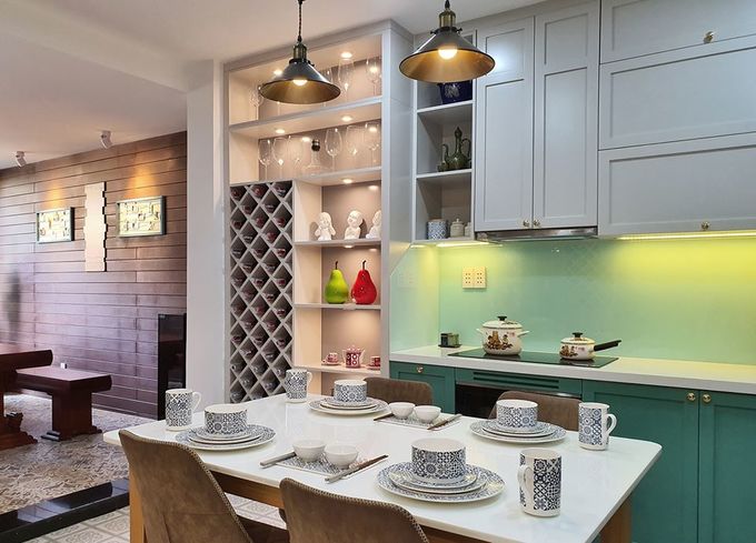Hình ảnh phòng bếp hiện đại với tủ bếp màu xanh ngọc, bàn ăn màu trắng, ghế ngồi bọc nệm, đèn trang trí, tủ kệ đựng rượu, cốc chén