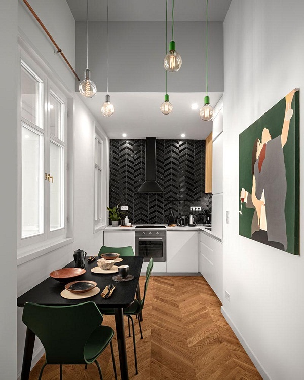 Hình ảnh trong phòng bếp căn hộ có gác lửng, nội thất được bài trí khá ấn tượng với tường ốp gạch đen bóng, ghế ăn màu xanh lá cùng tông với tranh treo tường nghệ thuật.