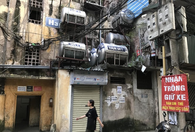 Hình ảnh cận cảnh mặt ngoài chung cư cũ Nguyễn Công Trứ với tường rêu mốc, dây điện chằng chịt, cô gái đi qua