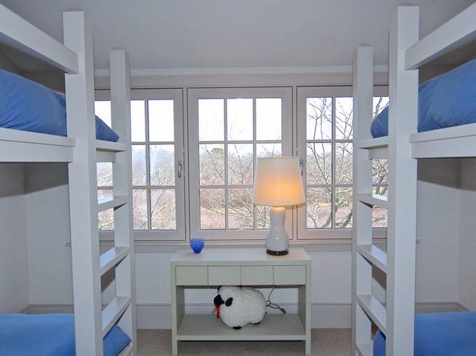 Hình ảnh phòng ngủ màu trắng với giường tầng, chăn nệm màu xanh, bàn gỗ, đèn ngủ