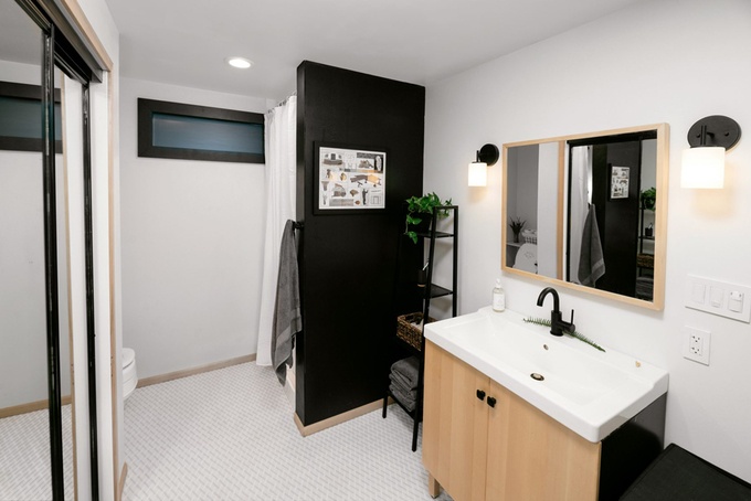Hình ảnh phòng tắm dưới gác xép với bồn rửa màu trắng, gương soi gắn tường, tủ gỗ, kệ thang màu đen