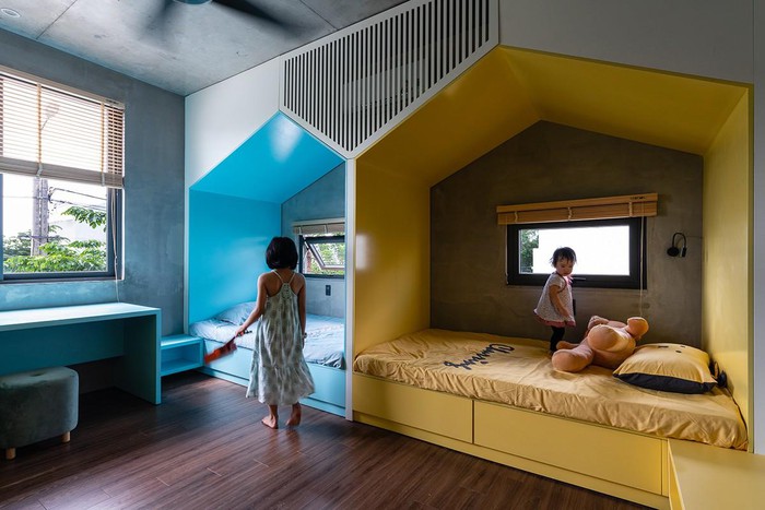 Hình ảnh hai bé gái trong phòng ngủ với giường hình ngôi nhà sơn màu xanh dương, vàng chanh, cửa kính