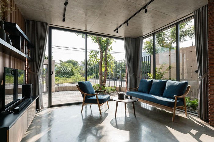 Hình ảnh phòng khách rộng thoáng với tường kính trong suốt, sofa bọc nệm xanh, tủ kệ tivi bằng gỗ, sân vườn xanh mát