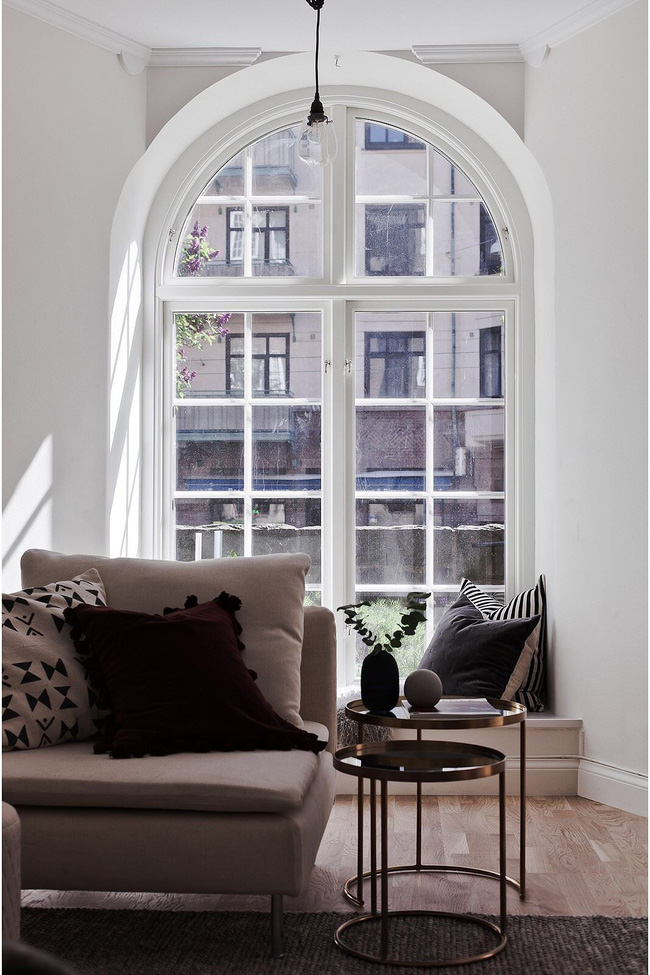 Hình ảnh cận cảnh một góc phòng khách với sofa trắng, gối tựa êm ái, khung cửa sổ kính hình vòm, bàn trà đôi