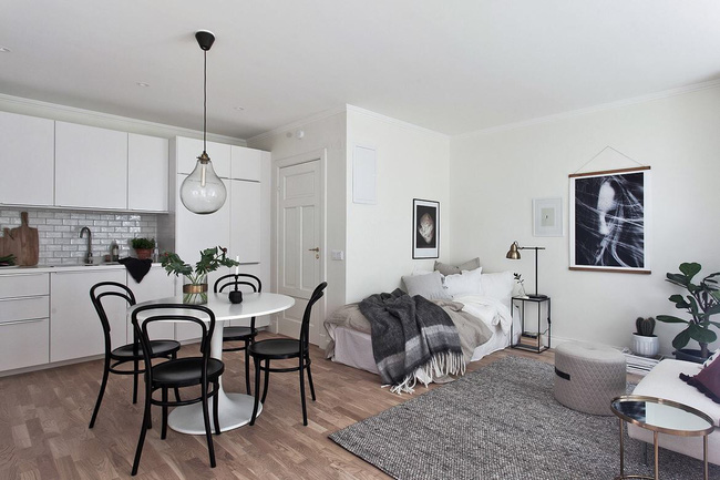 Hình ảnh một góc căn hộ 31m2 với tủ bếp màu trắng, bàn ăn tròn, ghế đen, sofa trắng, cây xanh