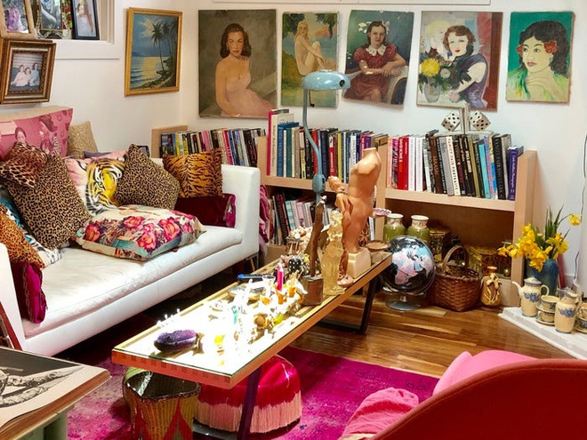 Hình ảnh phòng khách trong nhà màu hồng với tranh treo tường, giá sách, lọ hoa trang trí, thảm hồng