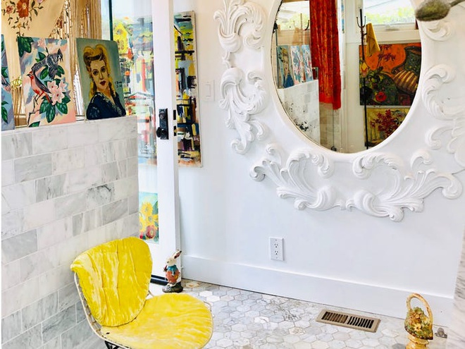 Hình ảnh một góc phòng tắm với ghế ngồi màu vàng, khung gương trang trí cầu kỳ, tranh vẽ treo tường