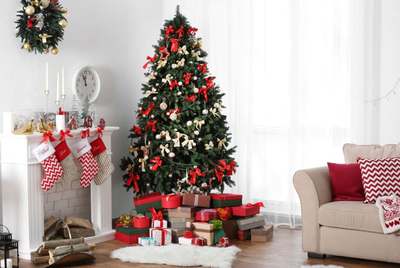 Hình ảnh cây thông Noel có nhiều nơ đỏ, quả cầu vàng, phía dưới có nhiều hộp quà, bên cạnh là lò sưởi, ghế sofa