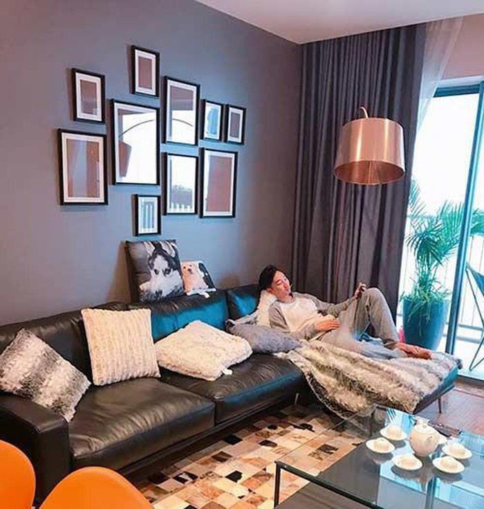 Hình ảnh MC Thành Trung nằm thư giãn trên ghế sofa da đen trong phòng khách, phía sau là bức tường màu tím, bộ tranh trang trí