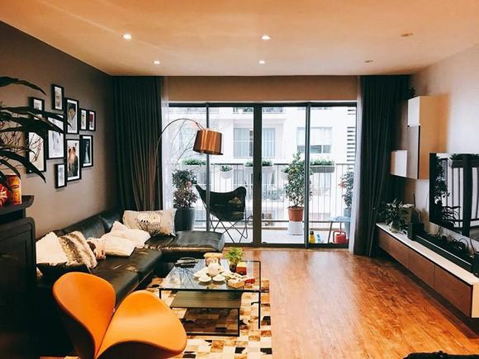 Hình ảnh toàn cảnh phòng khách căn hộ Thành Trung với sofa da den, bàn trà kính, bộ tranh treo tường, cây xanh trang trí, cửa sổ kính, rèm cửa