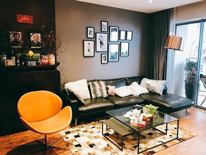 Toàn cảnh phòng khách với sofa da màu đen, bộ ảnh gia đình treo trên tường, cạnh đó là góc thờ cúng trang nghiêm, ghế thư giãn màu cam