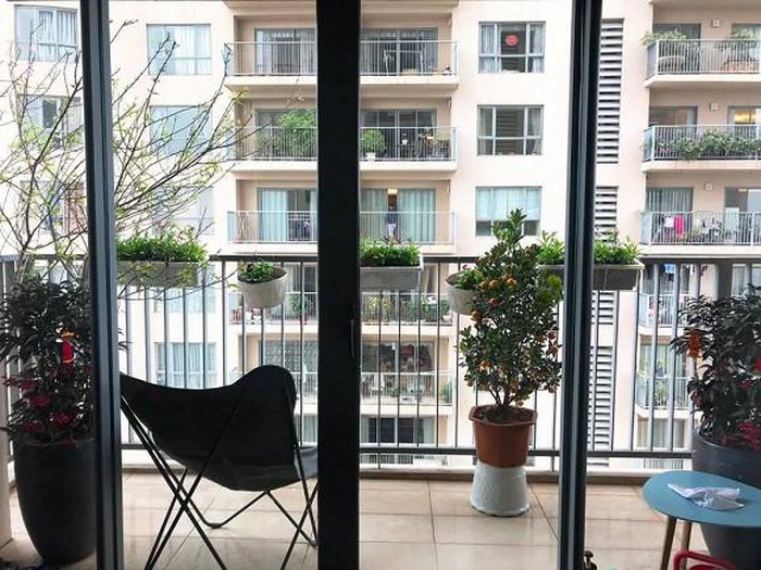 Hình ảnh ban công căn hộ được bài trí thành góc thư giãn với ghế ngồi êm ái, bàn trà nhỏ và những chậu cây xanh mướt gắn trực tiếp vào lan can