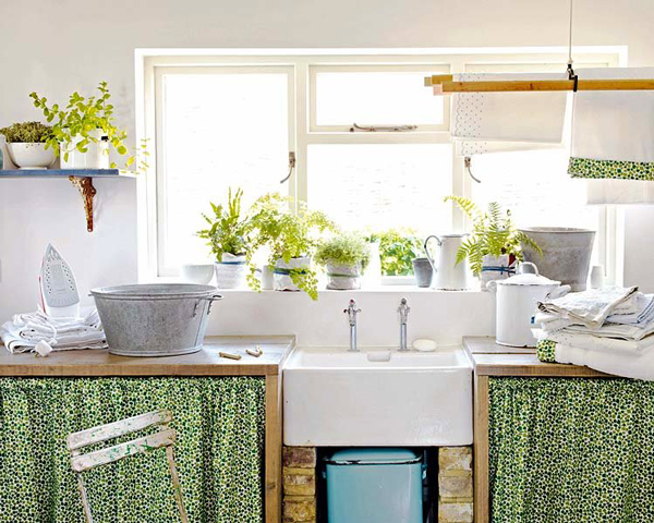 Hình narh một góc phòng bếp ngập tràn ánh sáng với những chậu cảnh xanh mướt đặt trên giá gắn tường, rèm che tủ bếp dưới